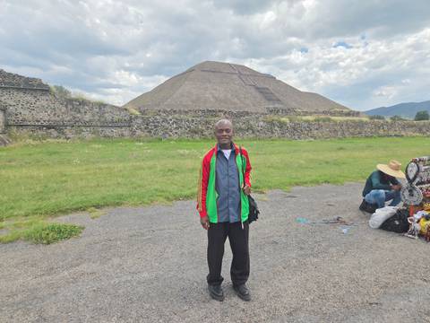 Visitor poses before the massive Pyramid of the Sun at Teotihuacan under a partly cloudy sky.
