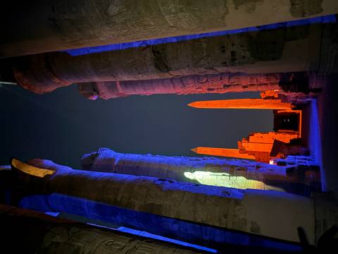 Nighttime view down a colonnaded temple corridor lit dramatically in blue and orange with two obelisks.