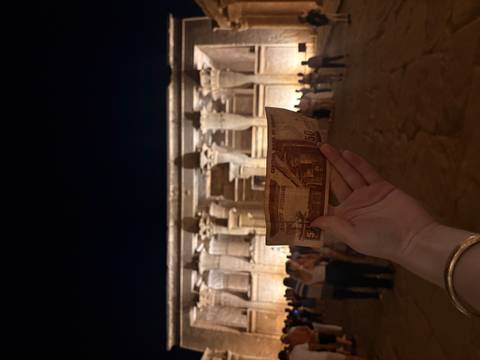 Hand holding an Egyptian 50-pound note matching the illuminated Kom Ombo Temple façade at night.