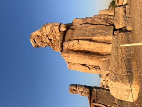 Colossus of Memnon statue illuminated by warm morning light under a clear blue sky.