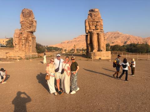 Travellers posing for a photo between the twin Colossi of Memnon statues with desert hills behind.