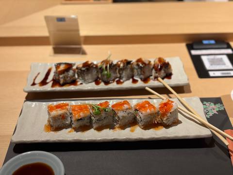 Artfully plated sushi rolls drizzled with sauce on ceramic trays with chopsticks