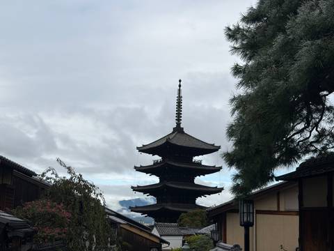 Five-storied wooden pagoda rising above traditional rooftops under a cloudy Kyoto sky