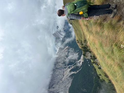 Hiker gazes over misty alpine valleys and jagged peaks from a grassy ridge