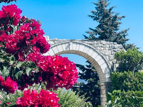 Stone arch framed by vibrant magenta bougainvillea flowers against a clear sky.