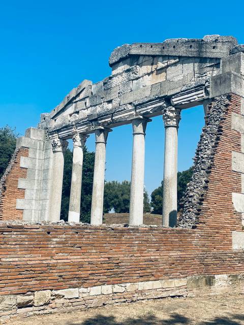 Ruins of an ancient Roman temple with intact marble columns against a bright blue sky.