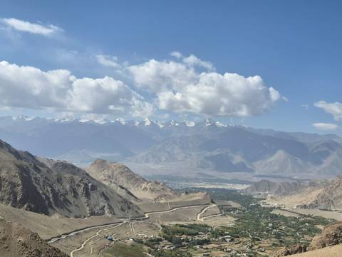 High mountain panorama with arid ridges and distant snowy peaks under scattered clouds