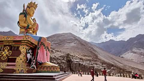 Large colourful Buddha statue overlooking mountain valley with visitors in foreground