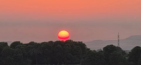 Large orange sun setting behind silhouette of treeline and distant hills