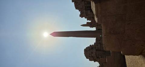 Tall ancient obelisk with sun perfectly aligned at the tip against clear blue sky