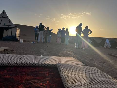 Silhouetted group chatting near camels at sunset in the desert camp.
