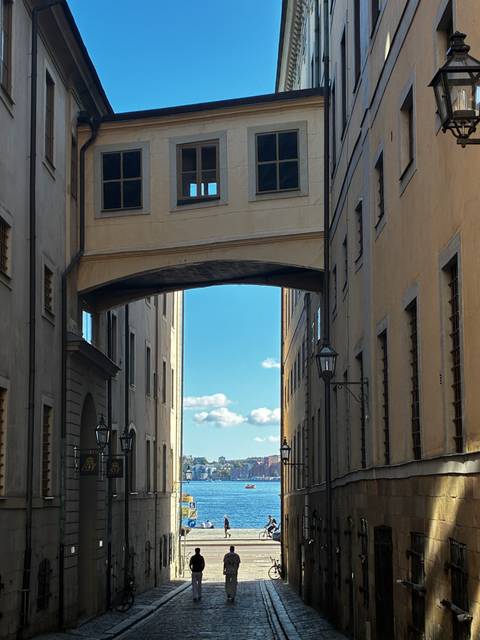 A narrow Stockholm street framed by tall buildings connected with an arched sky bridge.