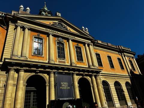 Facade of Stockholm’s orange-hued Nobel Prize Museum gleams against a deep blue sky.
