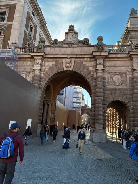 Crowds walk beneath a grand stone archway leading into Stockholm’s parliamentary district.