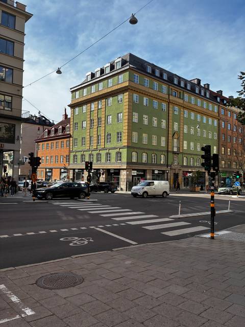 Busy Stockholm intersection with colorful historic buildings, cars and pedestrians at a crosswalk.