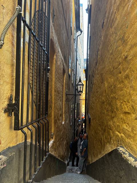 Extremely narrow stone alleyway with wrought-iron lamp between weathered golden walls.