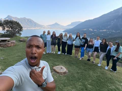 A playful selfie of a guide and tour group overlooking a vast lake and mountain slopes.