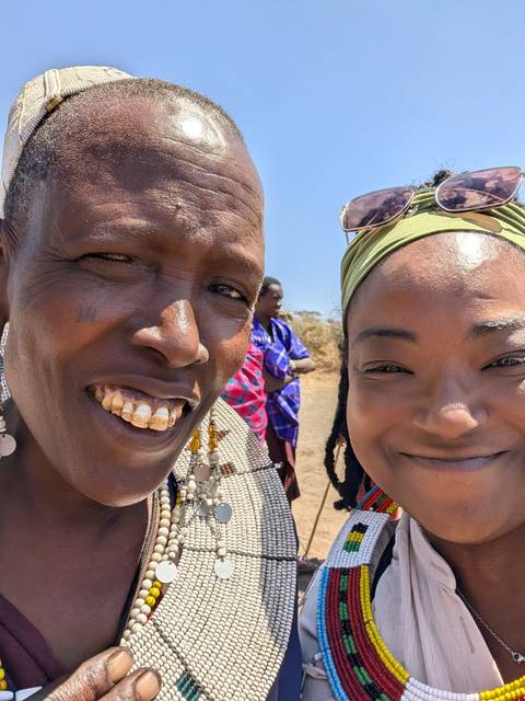 Close selfie of a traveler with a smiling Maasai woman in traditional attire.