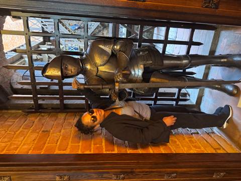 Traveler poses next to a medieval knight armor display inside a brick castle doorway.