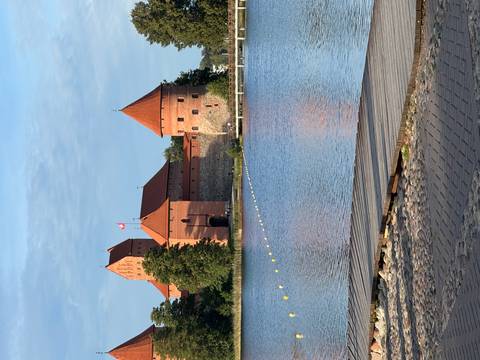Red-roofed Trakai Castle rises above a calm lake under blue skies.