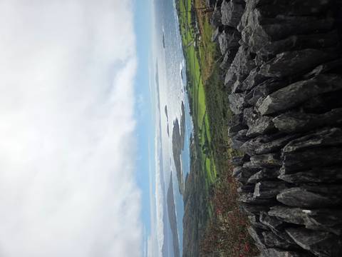 Atlantic coastline and green patchwork fields viewed over a stone wall on a cloudy day