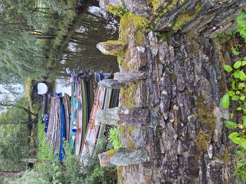 Row of wooden rowing boats moored on a calm narrow canal beside mossy stone wall