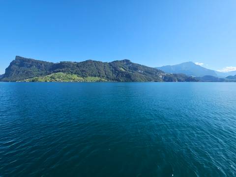 Deep-blue lake framed by forested slopes and distant alpine peaks under a cloudless sky
