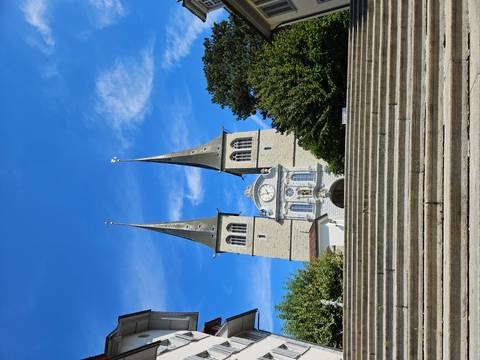 Twin-spired Church of St. Leodegar rises above wide stone steps under a vivid blue sky