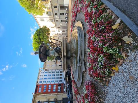 Decorative stone fountain encircled by colourful flowerbeds in a sunny urban square