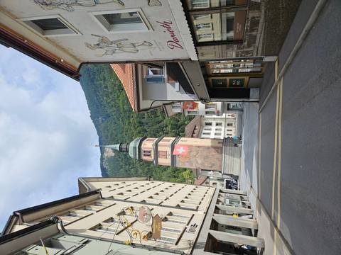 Quiet Swiss village street featuring a tower painted with the national flag and forested hills behind