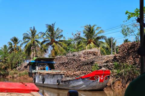 Small cargo boat moored along a Mekong Delta canal flanked by coconut palms and stacks of timber.