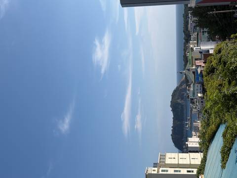 Coastal cityscape of Jeju with distant volcanic isle under a clear blue sky.