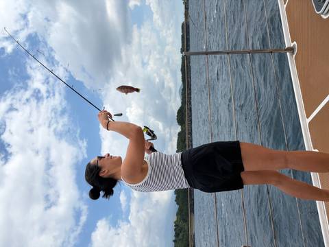 Young woman reeling in a fish while standing on a yacht deck on open sea.