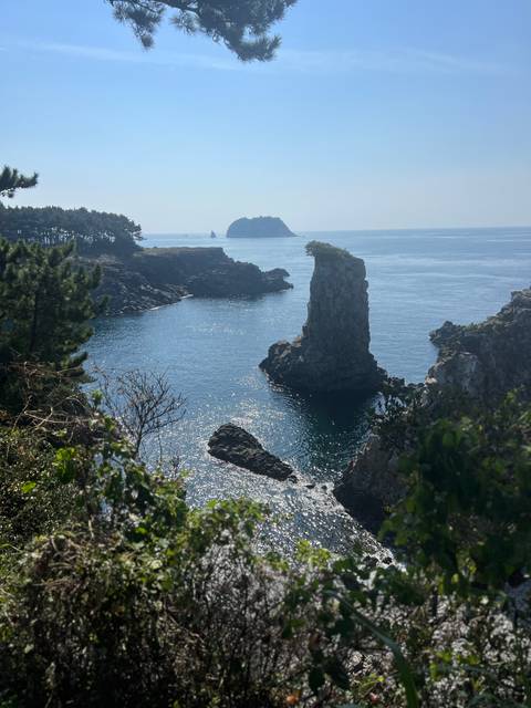 Dramatic sea stack and sparkling blue water off rugged Jeju Island coastline.