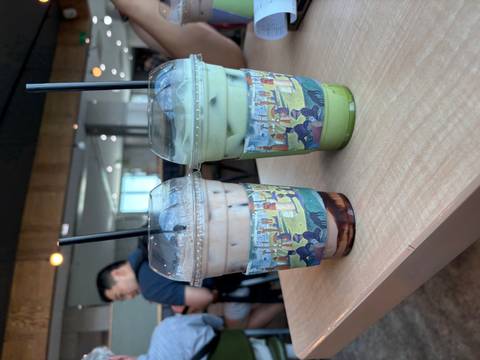 Two iced drinks, one chocolate and one matcha, rest on a cafe table with a patron blurred behind.