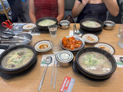 Steaming bowls of Korean soup with assorted side dishes arranged on a wooden restaurant table.