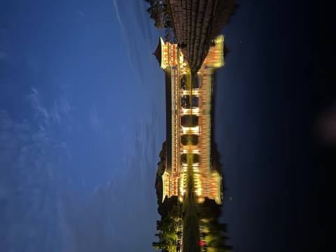 Illuminated traditional covered bridge reflected perfectly on still water against a deep blue evening sky.
