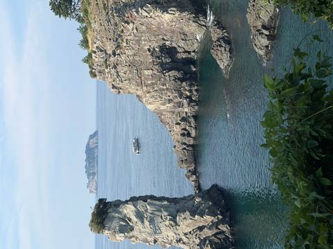 Rugged volcanic cliffs enclose a calm turquoise cove with a small offshore island on the horizon.