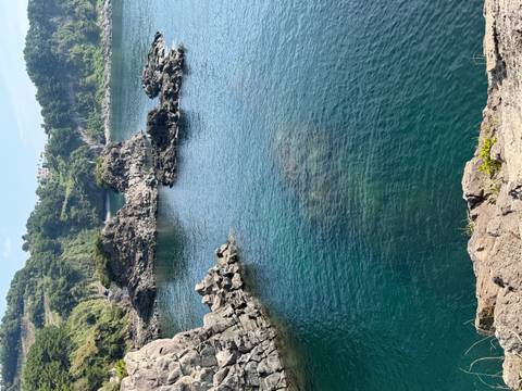 Clear blue water fills a rocky volcanic inlet surrounded by rugged black formations.
