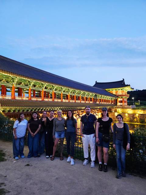 Smiling tour group posing in front of an ornately lit wooden bridge at dusk.