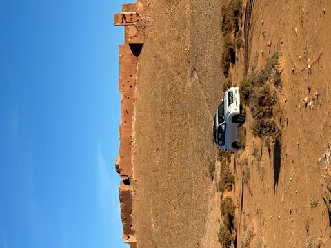 A white SUV parked on barren desert ground with an old clay fortress wall in the distance.