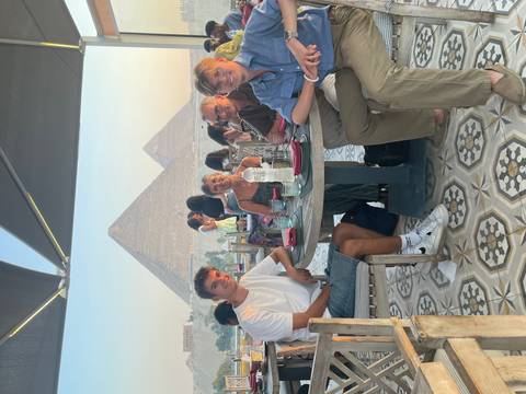 Family dining at a rooftop restaurant with two iconic pyramids of Giza towering in the hazy background at golden hour.