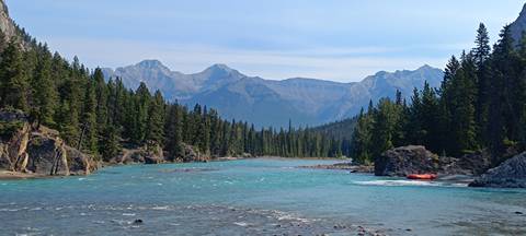 Turquoise river winding through pine forest with inflatable raft on shore