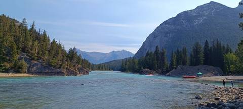Wide alpine river flowing through conifer forest with mountains framing the valley