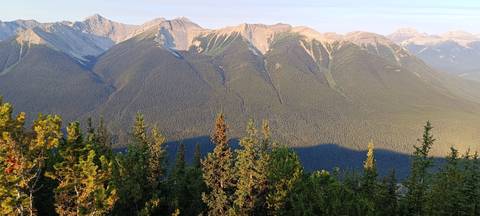 Sunlit ridgeline of forested mountains with evening shadows across the valley