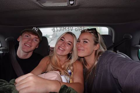 Three friends smile for a selfie while seated inside a vehicle.