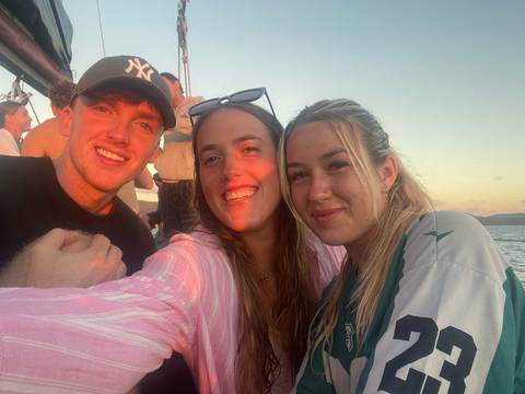 Three friends pose on a boat deck at sunset with soft golden light on their faces.