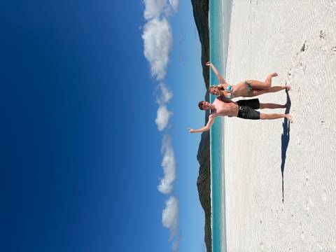 Couple celebrate on the white silica sands of Whitehaven Beach with crystal-clear turquoise water behind.