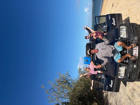 Tour guide and travellers enthusiastically pose with arms outstretched on a 4x4 tour vehicle.