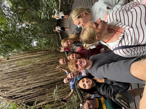 Travellers pose for a selfie along a rainforest boardwalk beside massive hanging roots.